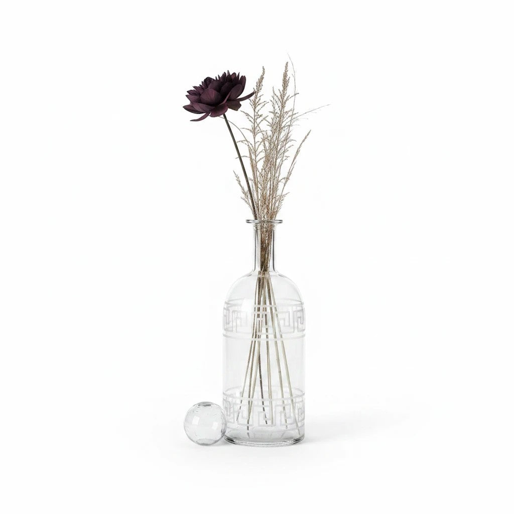 The House of Saffron clear glass vase with white geometric patterns holding a dark flower and dried grass stems.