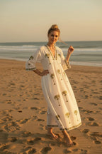 The House of Saffron white midi dress with olive green palm tree embroidery, V-neckline, and flowy silhouette on beach
