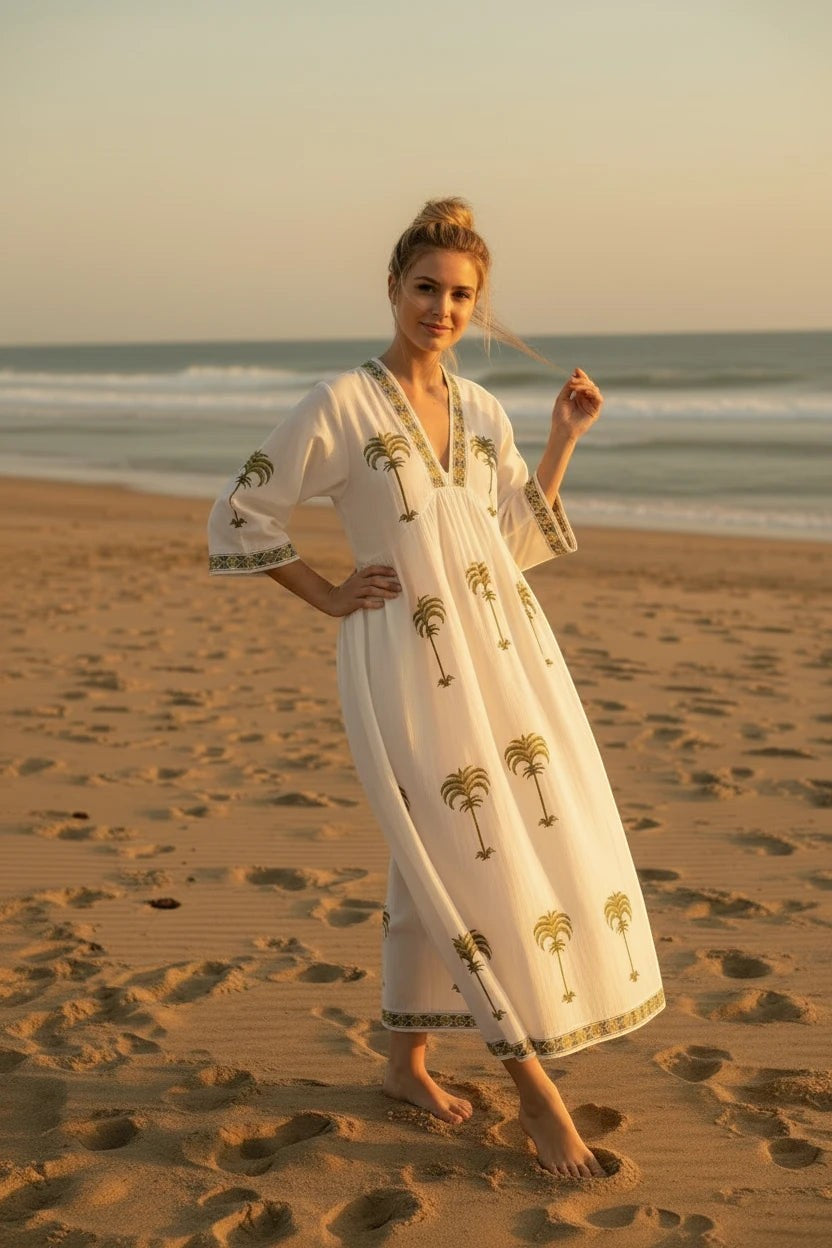 The House of Saffron white midi dress with olive green palm tree embroidery, V-neckline, and flowy silhouette on beach